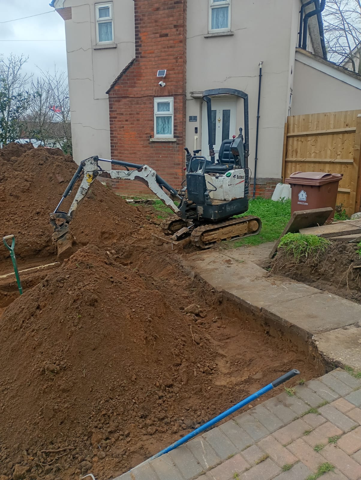 Mini excavator digging a drainage trench alongside a residential property